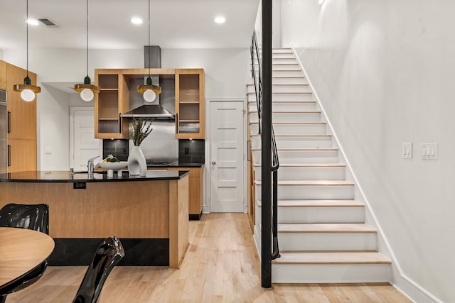 kitchen with wall chimney exhaust hood, tasteful backsplash, decorative light fixtures, light hardwood / wood-style flooring, and a kitchen breakfast bar