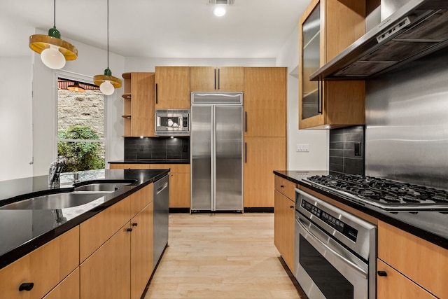 kitchen featuring pendant lighting, sink, light hardwood / wood-style flooring, built in appliances, and wall chimney exhaust hood