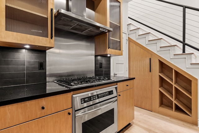 kitchen featuring wall chimney range hood, decorative backsplash, light hardwood / wood-style floors, and appliances with stainless steel finishes