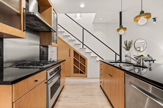 kitchen with appliances with stainless steel finishes, sink, hanging light fixtures, light hardwood / wood-style floors, and wall chimney exhaust hood