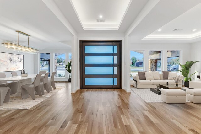 living room with a tiled fireplace, light wood-type flooring, and a tray ceiling