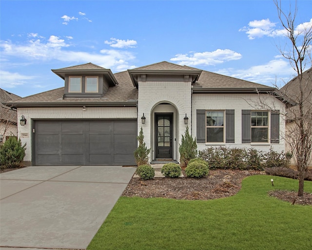 view of front of property with a front yard, an attached garage, a shingled roof, concrete driveway, and brick siding