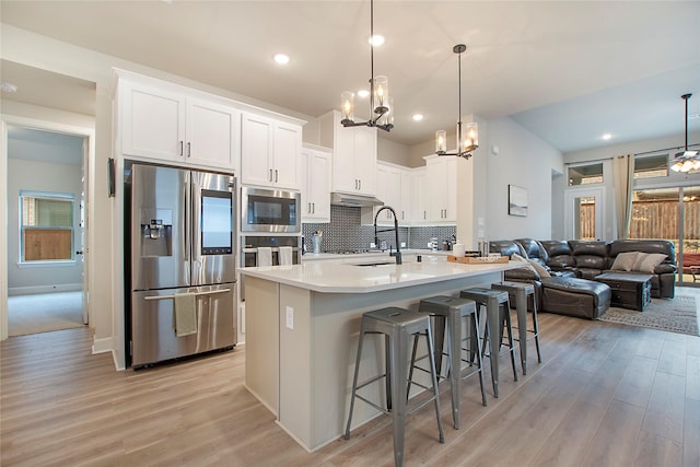 kitchen featuring pendant lighting, sink, stainless steel appliances, white cabinets, and a kitchen bar