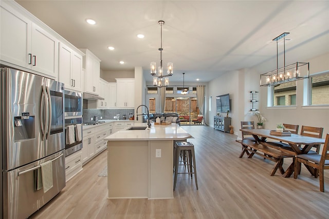 kitchen featuring sink, decorative light fixtures, appliances with stainless steel finishes, a kitchen island with sink, and white cabinets