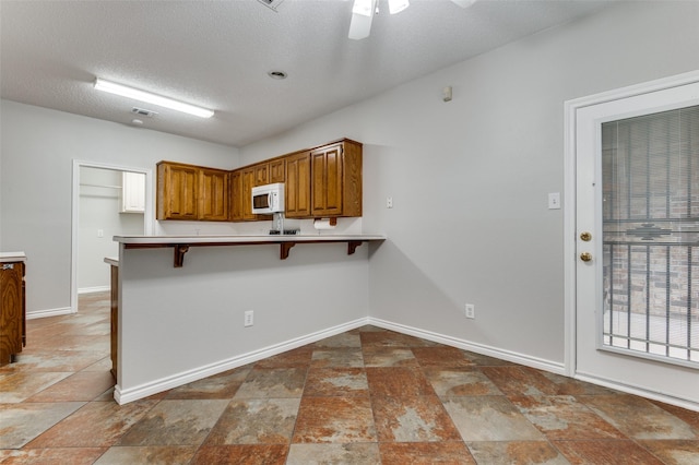 1230 Wooded Trl, Hurst, TX 76053 - kitchen featuring white microwave, ceiling fan, brown cabinetry, a peninsula, and baseboards