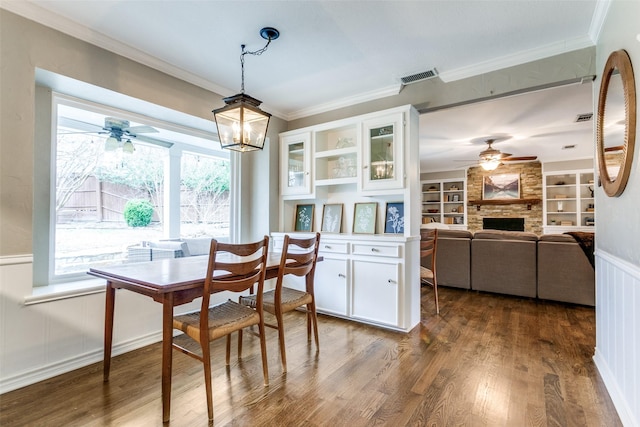 dining space featuring crown molding, a stone fireplace, dark hardwood / wood-style floors, and ceiling fan