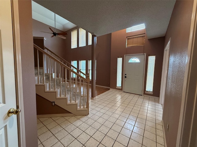 entryway featuring ceiling fan, a towering ceiling, light tile patterned floors, and a textured ceiling