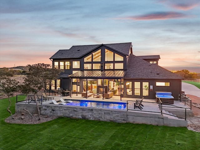 back house at dusk featuring a patio, outdoor lounge area, pool water feature, and a lawn