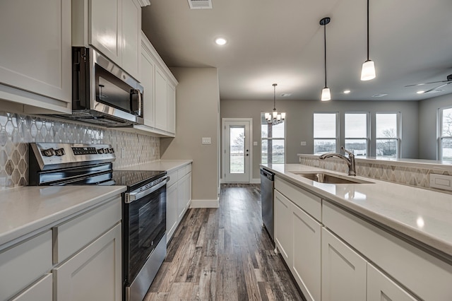 kitchen featuring stainless steel appliances, sink, white cabinets, and decorative light fixtures