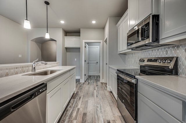 kitchen featuring appliances with stainless steel finishes, sink, white cabinets, decorative backsplash, and hanging light fixtures