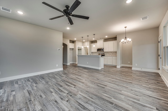 unfurnished living room with ceiling fan with notable chandelier and light wood-type flooring