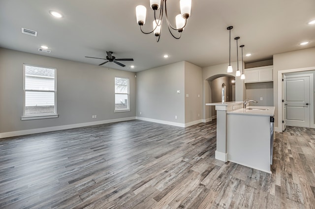 kitchen featuring ceiling fan with notable chandelier, white cabinetry, wood-type flooring, a center island with sink, and decorative light fixtures