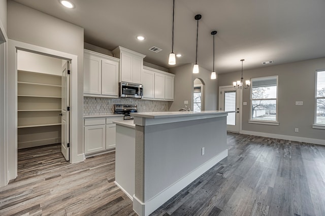 kitchen with a center island with sink, stainless steel appliances, hanging light fixtures, and white cabinets