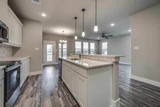 kitchen with appliances with stainless steel finishes, decorative light fixtures, sink, white cabinets, and a kitchen island with sink