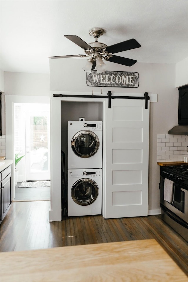 clothes washing area with dark wood-type flooring, ceiling fan, a barn door, and stacked washing maching and dryer