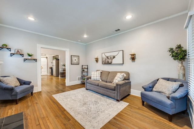 living area featuring wood finished floors, visible vents, crown molding, and baseboards