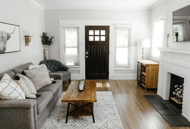 living room with crown molding, a brick fireplace, hardwood / wood-style flooring, and plenty of natural light