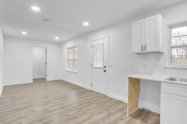 kitchen with tasteful backsplash, a healthy amount of sunlight, white cabinets, and light wood-type flooring