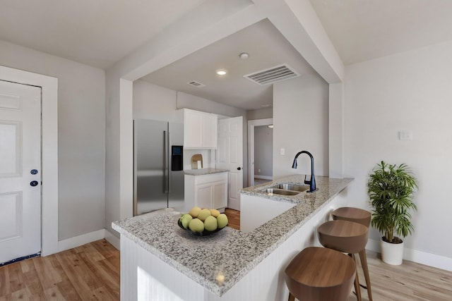 kitchen with sink, white cabinets, a kitchen breakfast bar, kitchen peninsula, and high end fridge