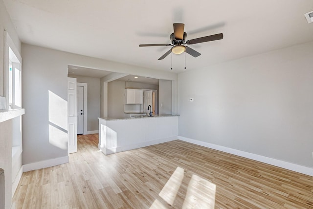 unfurnished living room featuring ceiling fan, sink, and light wood-type flooring