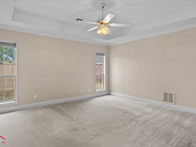 empty room with a tray ceiling, ornamental molding, light colored carpet, and ceiling fan