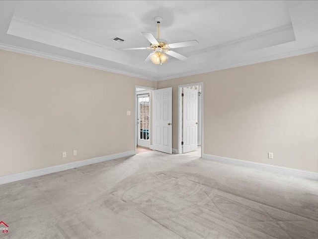 empty room featuring a raised ceiling, ornamental molding, light carpet, and ceiling fan