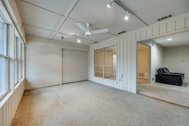 unfurnished room featuring ceiling fan, brick wall, rail lighting, and carpet floors