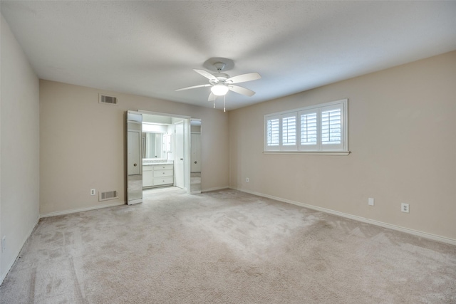 unfurnished bedroom with ceiling fan, light colored carpet, and ensuite bathroom