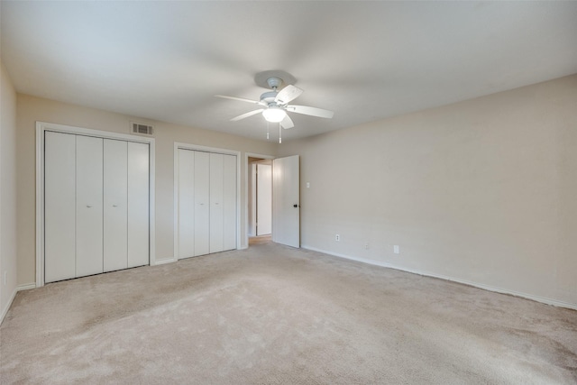 unfurnished bedroom featuring multiple closets, ceiling fan, and light carpet