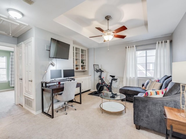 office space featuring ceiling fan, light colored carpet, and a raised ceiling