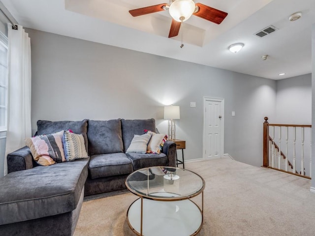 living room with light colored carpet, a raised ceiling, and ceiling fan