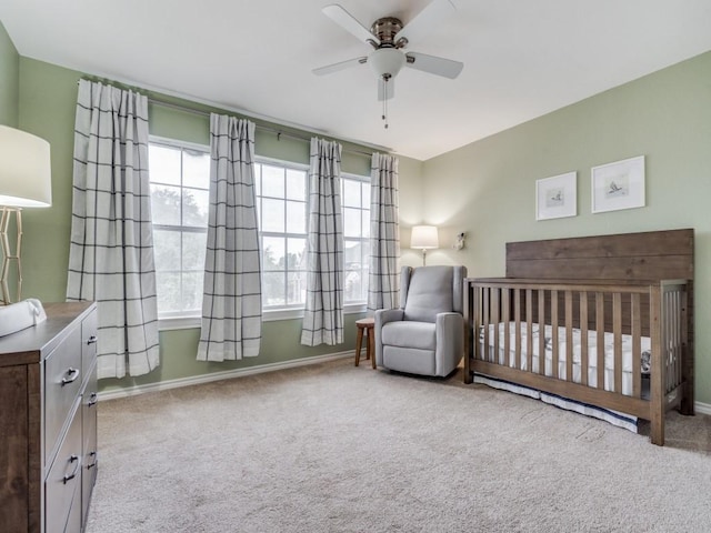 carpeted bedroom with a crib and ceiling fan