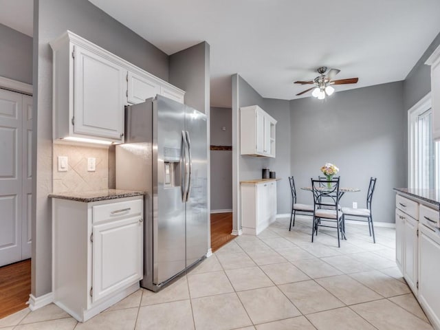 kitchen with light tile patterned floors, ceiling fan, stainless steel refrigerator with ice dispenser, white cabinets, and dark stone counters