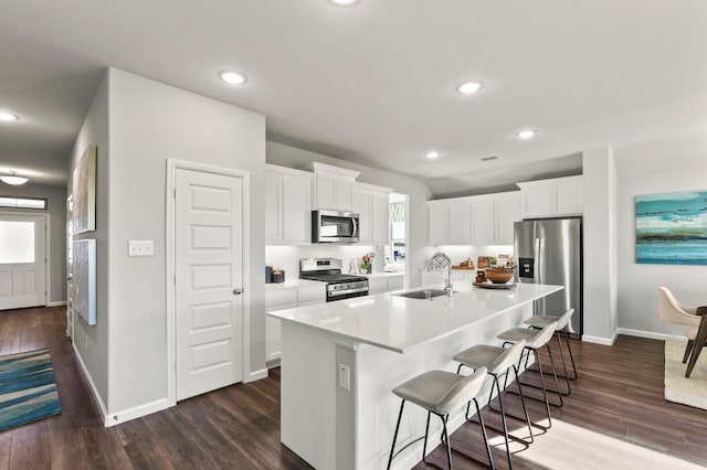 kitchen with sink, a breakfast bar area, stainless steel appliances, an island with sink, and white cabinets