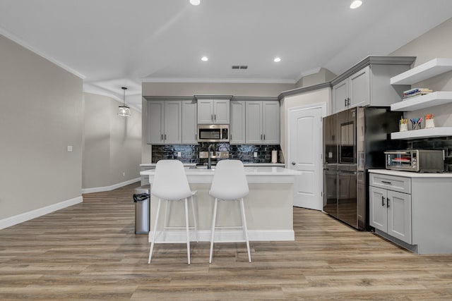 kitchen featuring decorative backsplash, stainless steel appliances, a center island with sink, and gray cabinetry