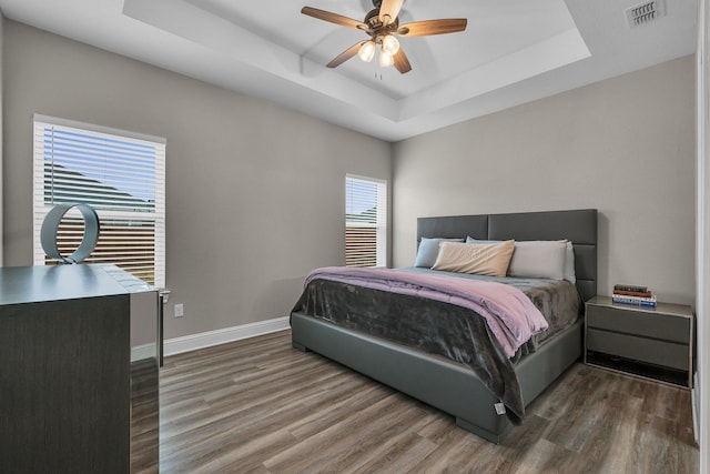 bedroom with dark wood-type flooring, a raised ceiling, and ceiling fan