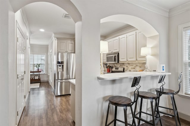 kitchen with dark hardwood / wood-style flooring, ornamental molding, appliances with stainless steel finishes, and a kitchen breakfast bar