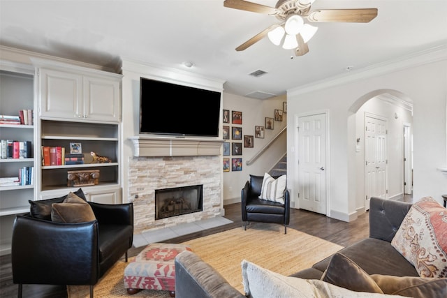 living room featuring a stone fireplace, wood-type flooring, ornamental molding, and ceiling fan