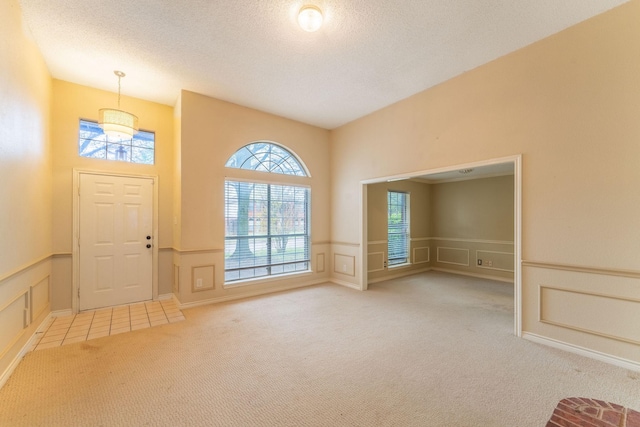 carpeted foyer featuring wainscoting, a decorative wall, a textured ceiling, and tile patterned floors