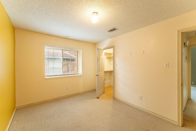 unfurnished bedroom featuring a closet, visible vents, light carpet, a textured ceiling, and baseboards