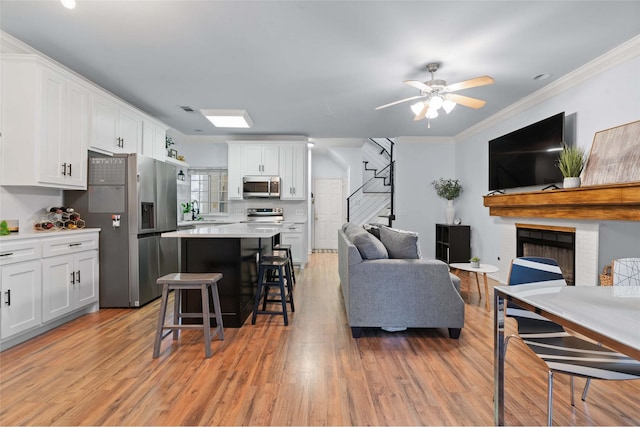 living room with crown molding, a fireplace, ceiling fan, and light wood-type flooring