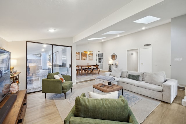 living room featuring vaulted ceiling with skylight and light hardwood / wood-style flooring