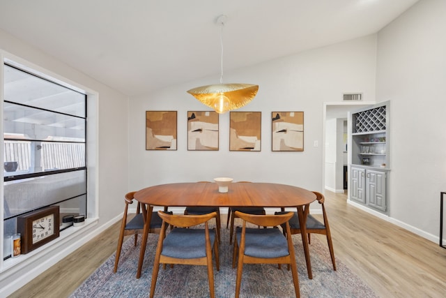 dining area featuring indoor bar, lofted ceiling, and wood-type flooring