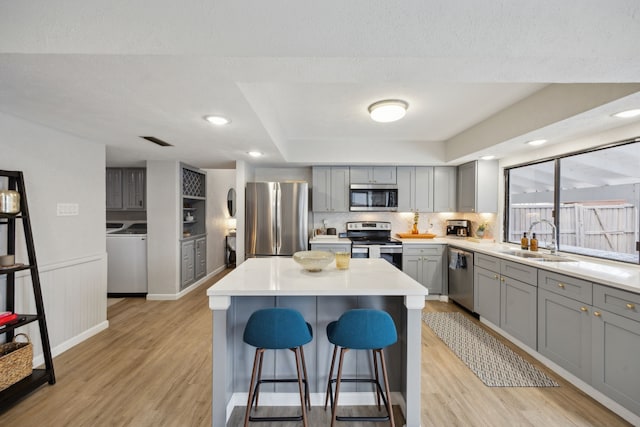 kitchen featuring washer and dryer, sink, gray cabinetry, a center island, and stainless steel appliances