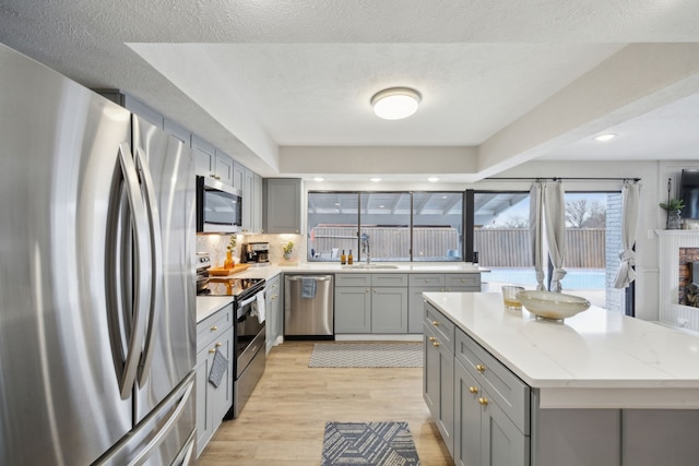 kitchen featuring sink, light hardwood / wood-style flooring, appliances with stainless steel finishes, a kitchen island, and light stone countertops