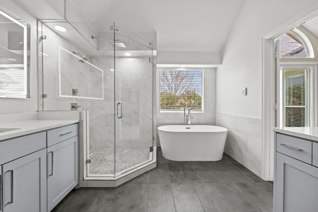 full bathroom with tile walls, wainscoting, vanity, a shower stall, and a freestanding tub