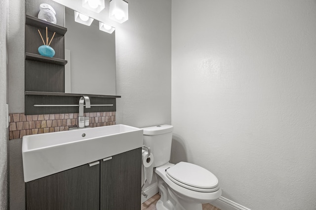 half bathroom featuring toilet, vanity, and a textured wall