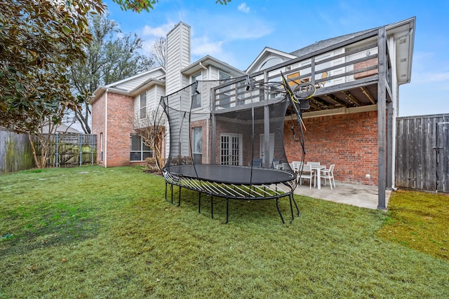 rear view of property with a yard, a patio, brick siding, and a trampoline