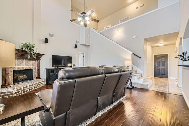 living room featuring ceiling fan, a fireplace, hardwood / wood-style floors, and a high ceiling