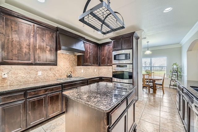 kitchen featuring appliances with stainless steel finishes, decorative light fixtures, dark stone countertops, and wall chimney exhaust hood